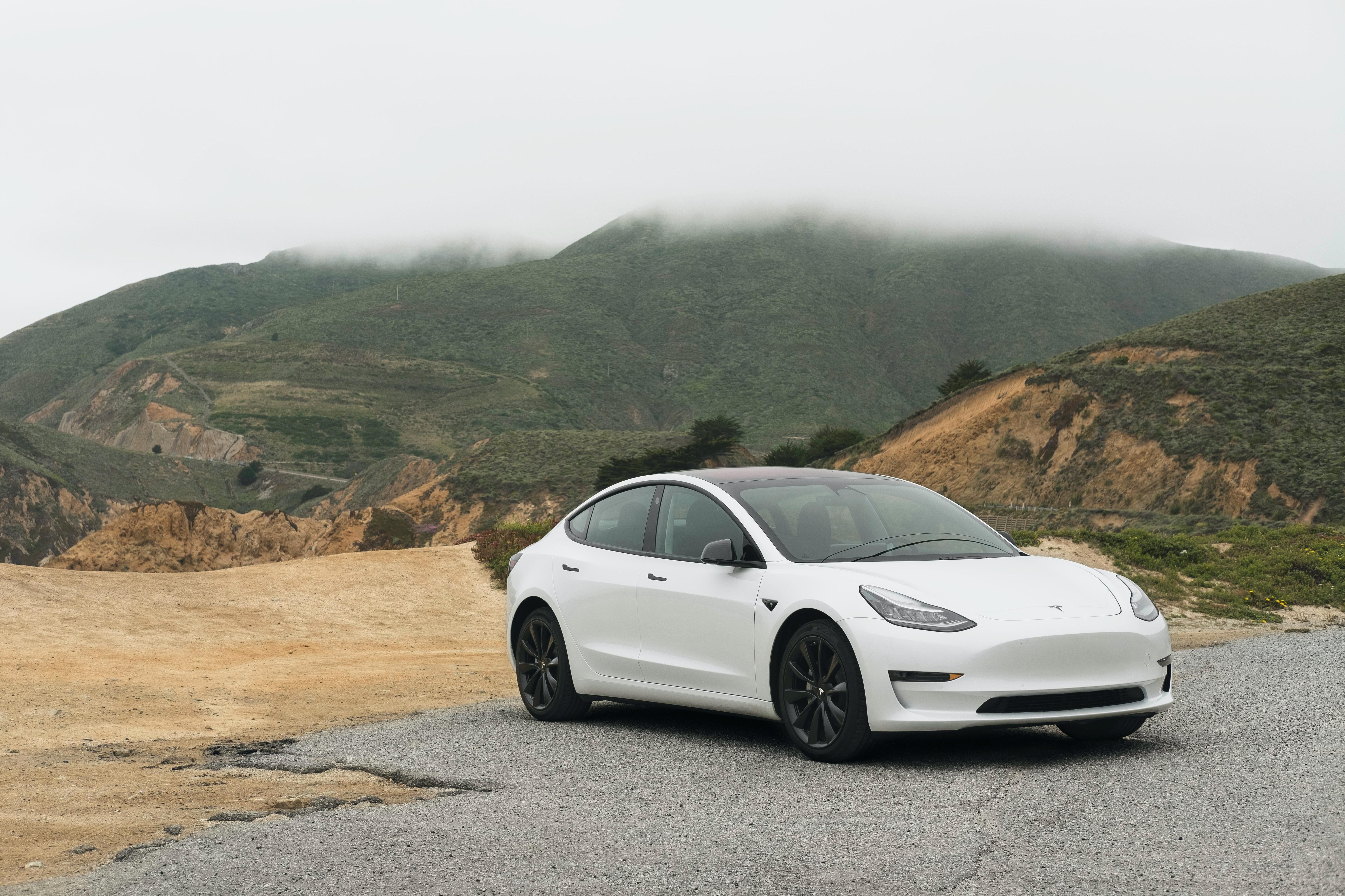 Fehér Tesla fekete alufelnikkel egy dombos vidéken, felhős időben