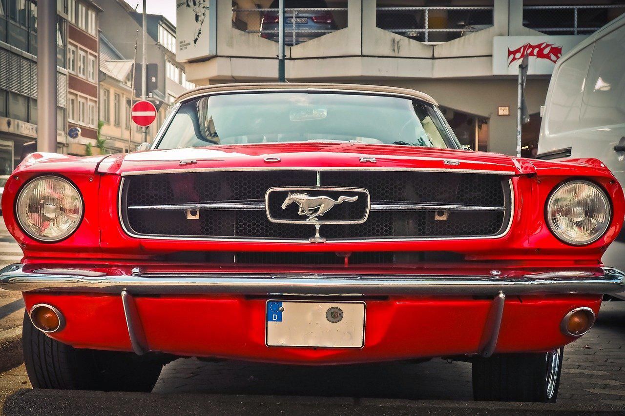 Piros Ford Mustang áll a parkolóban házak között nappal