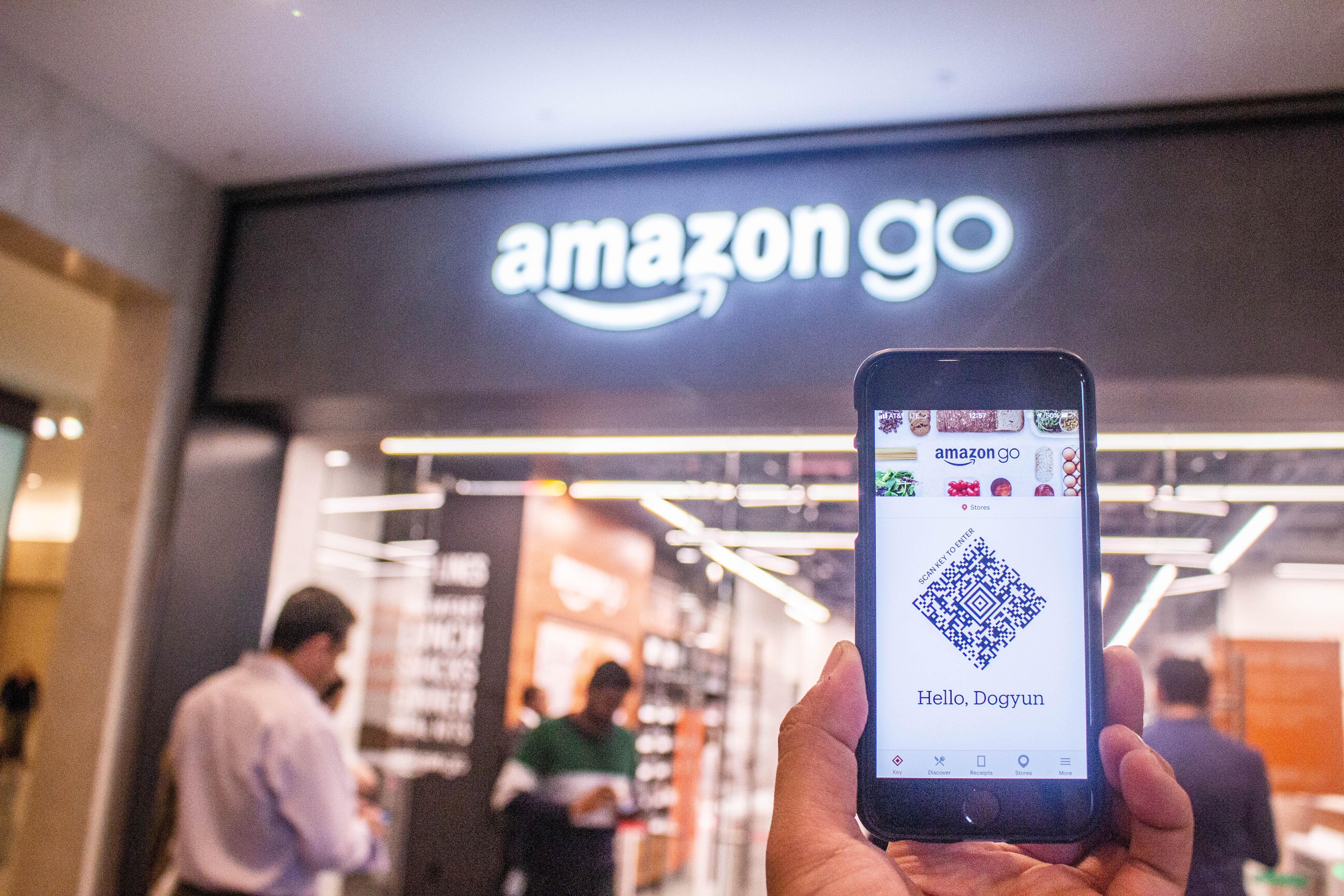Egy ember a telefonját tartja a kezében, amelyen az Amazon Go applikációja van megnyitva az Amazon Go fizikai boltja előtt