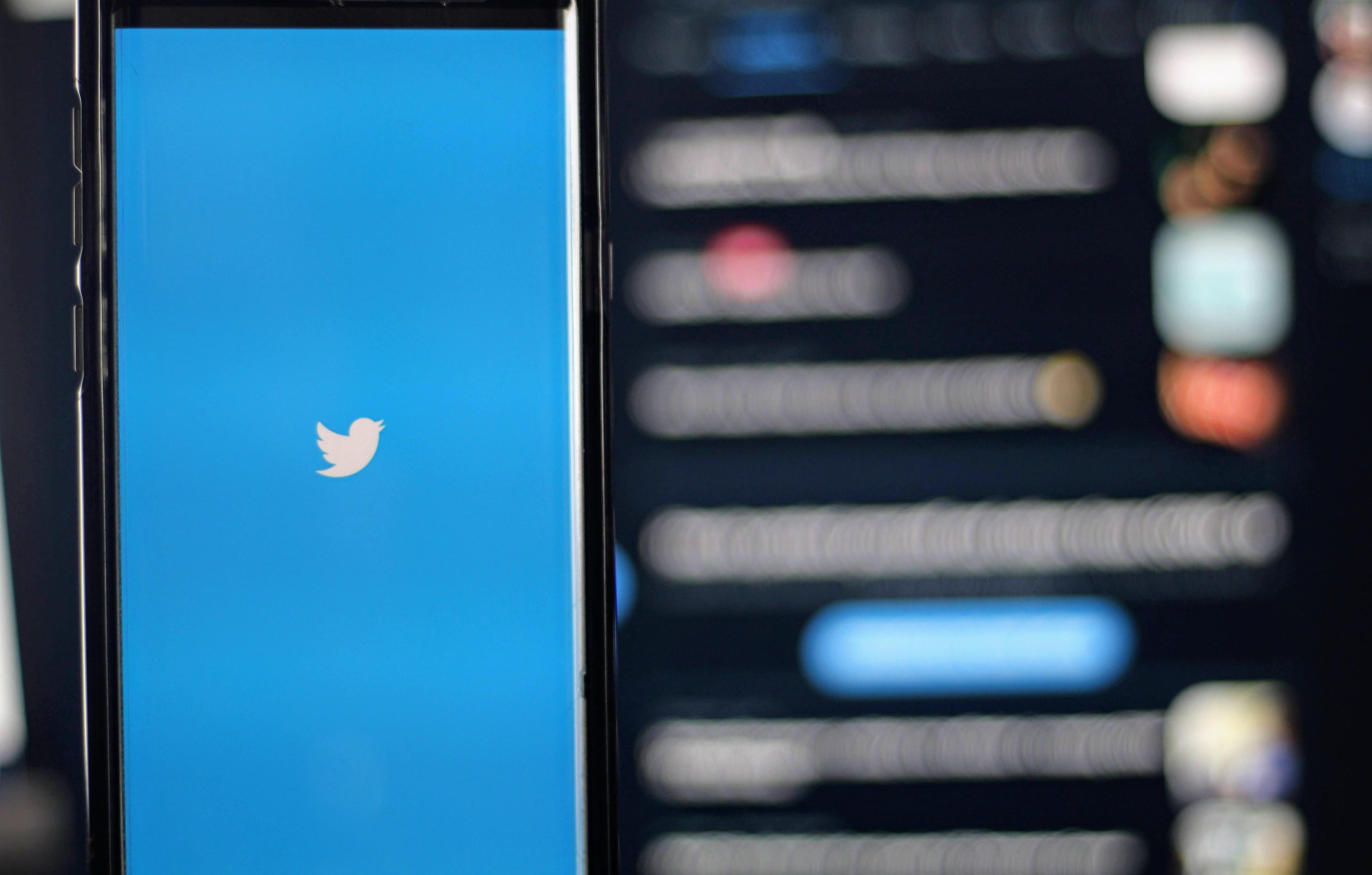 A Twitter logója (fehér madár kék alapon) látható egy okostelefon képernyőjén homályos háttér előtt
