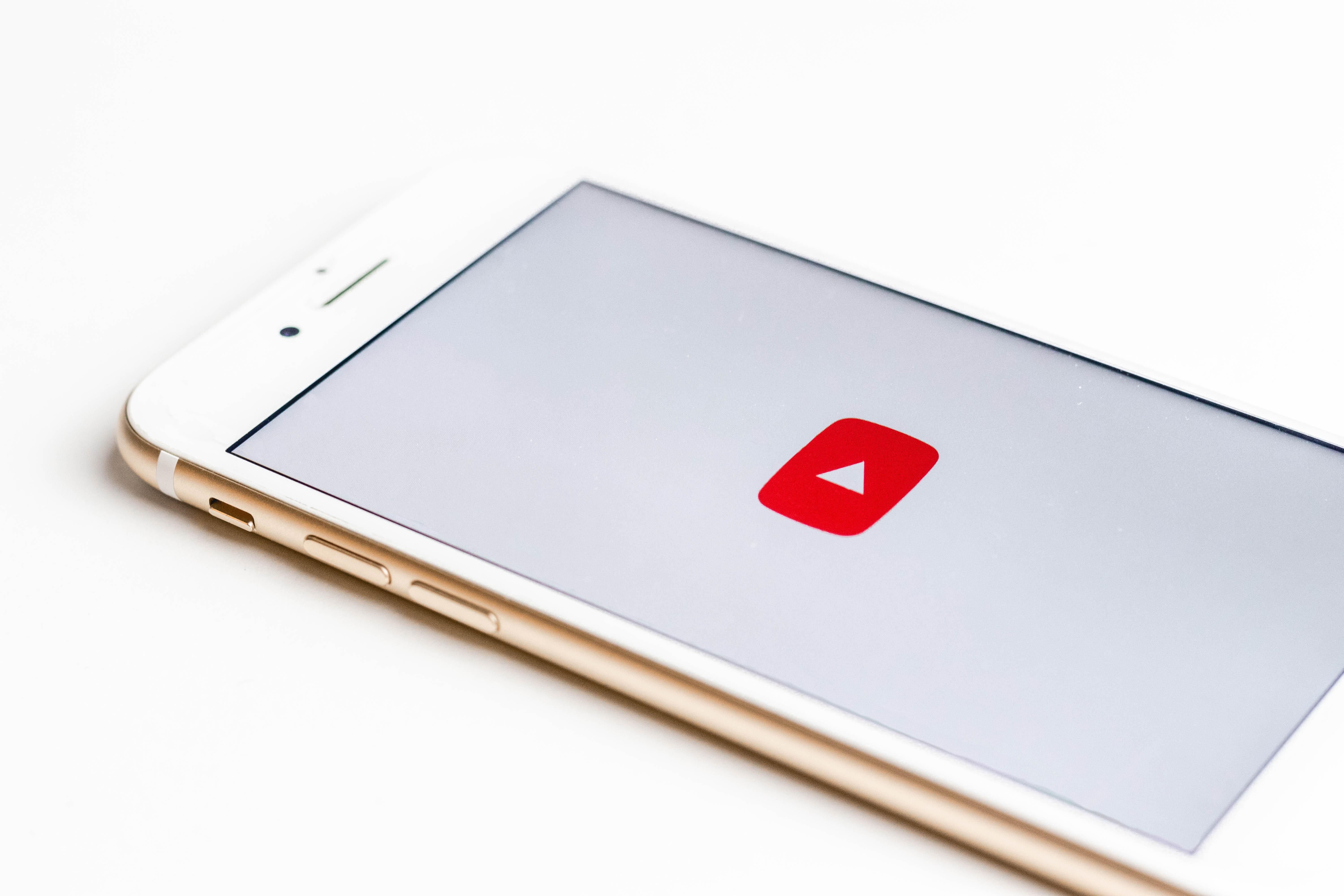 Rosegold színű okostelefonon valaki épp megnyitotta a YouTube alkalmazást, a háttér fehér