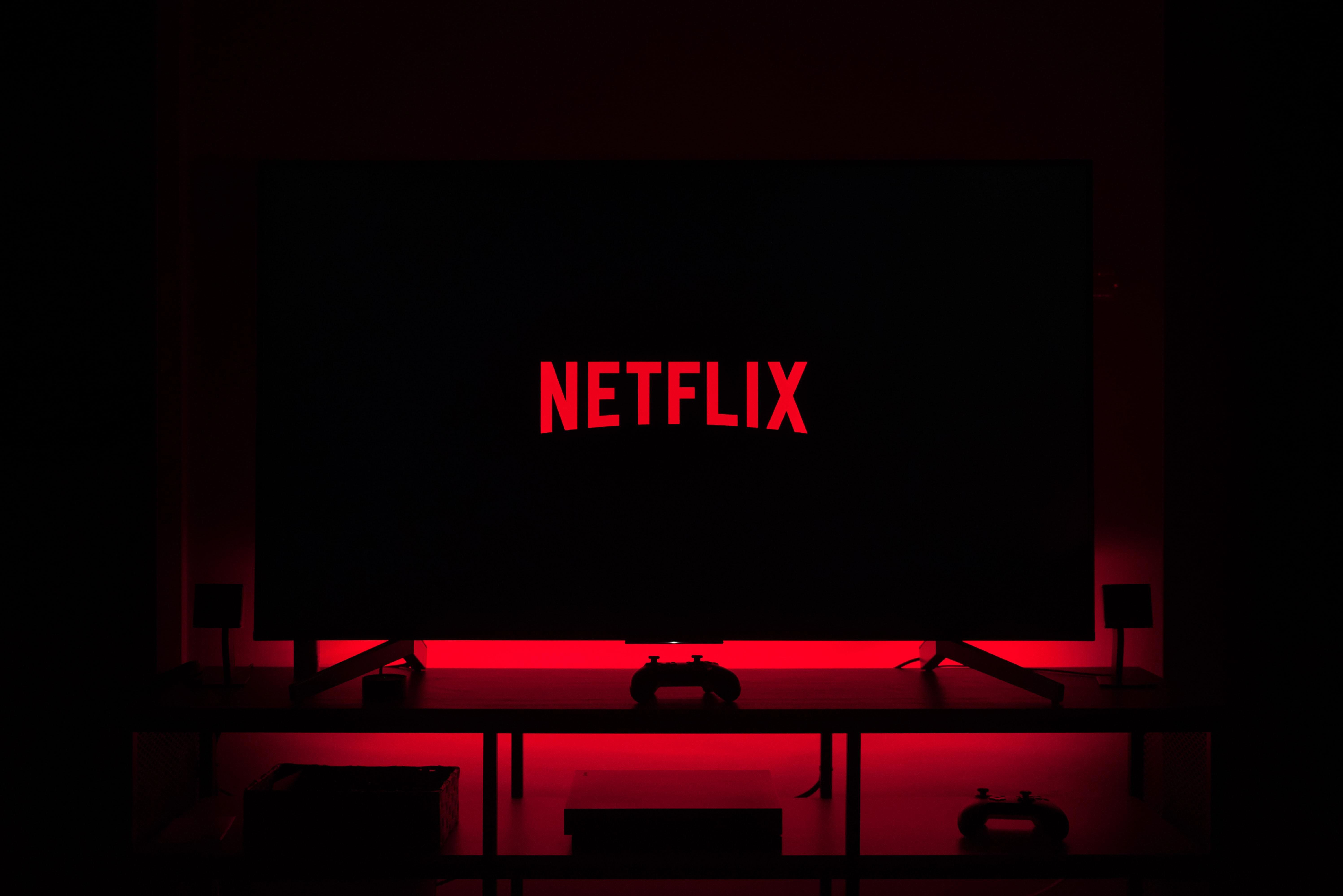 A Netflix logója látható egy okostévén, ami egy sötét szobában piros fényekkel van kivilágítva 
