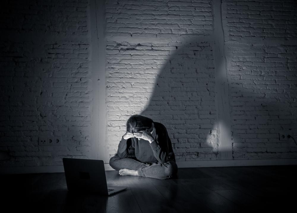 Fiatal lány egy sötét szobában szomorkodik a laptopja előtt ülve, miután gyűlöletbeszéd célpontjává vált