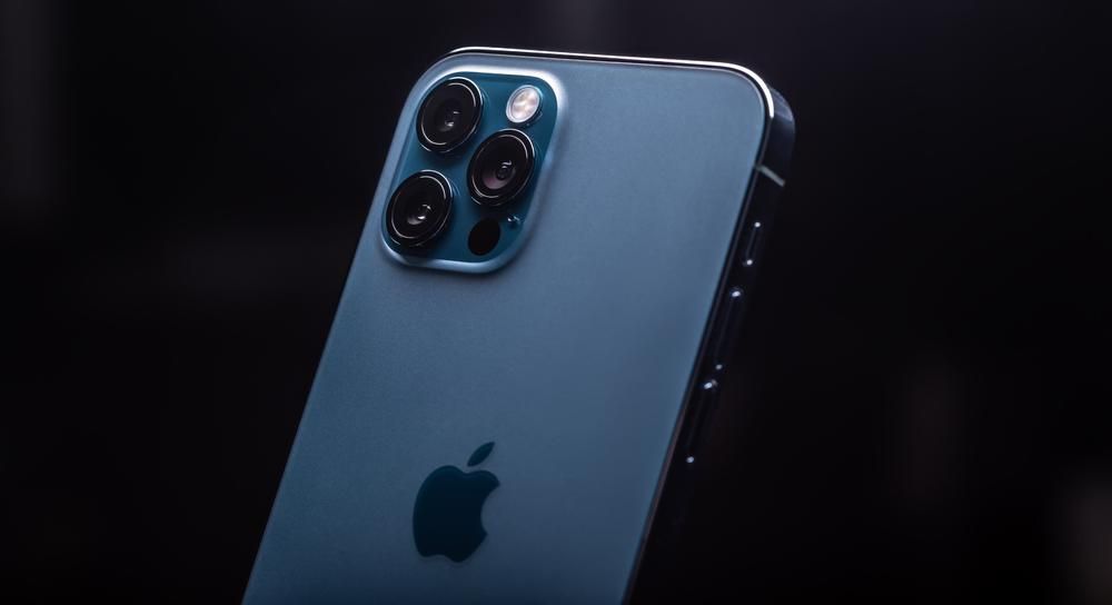 Az Apple egyik világoskék, három kamerás iPhone készüléke egy sötét szobában