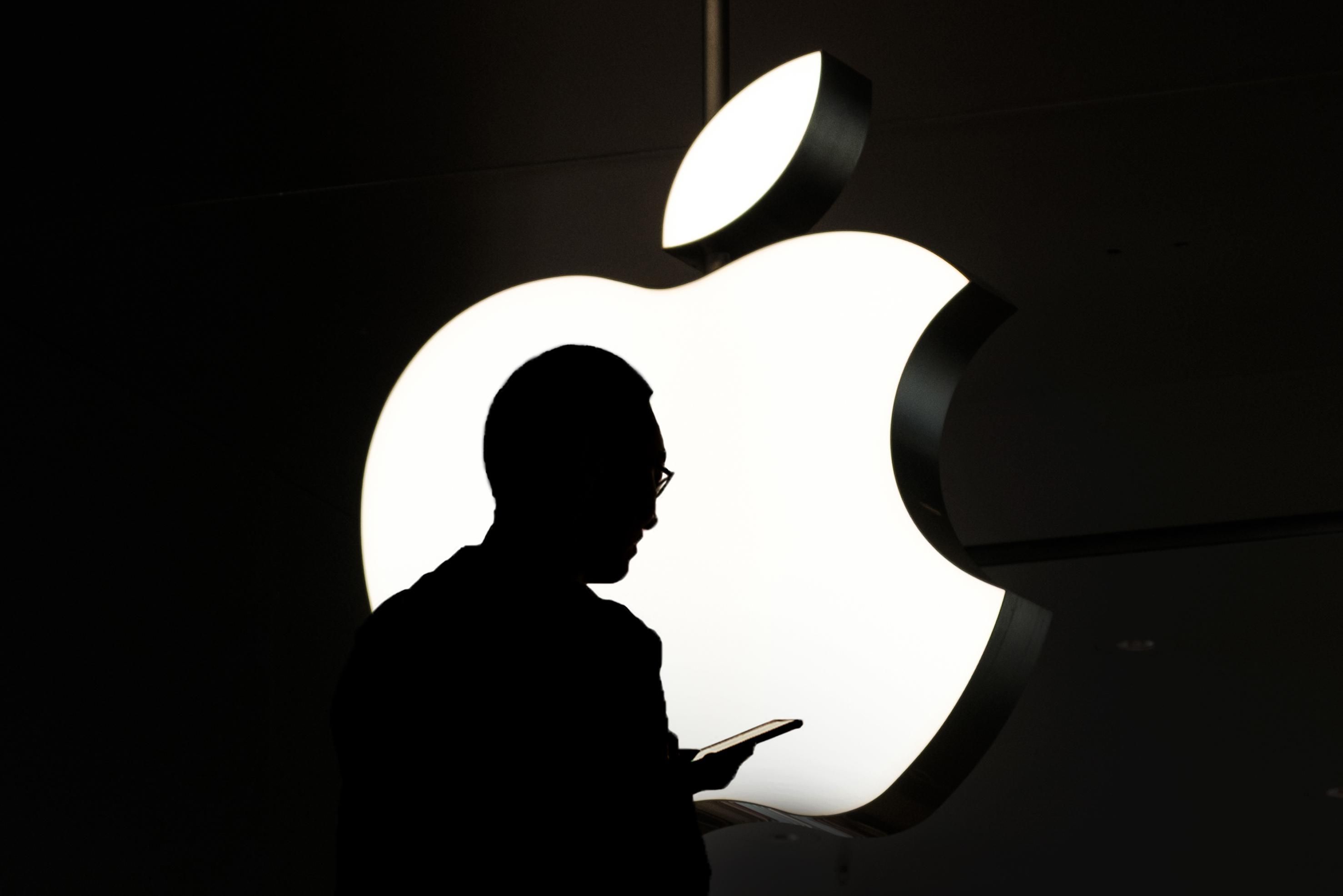 Egy telefonozó ember sziluettje látható háttérben az Apple logójával