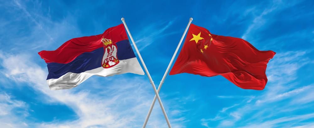 A szerb és a kínai zászlók egymást keresztezve lobognak a felhős, kék ég alatt