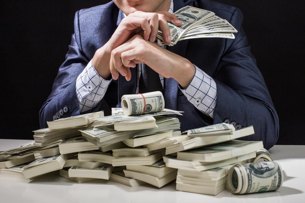 Egy kék öltönyös kripto-szakértő egy fehér asztalon könyököl, amin rengeteg pénz található