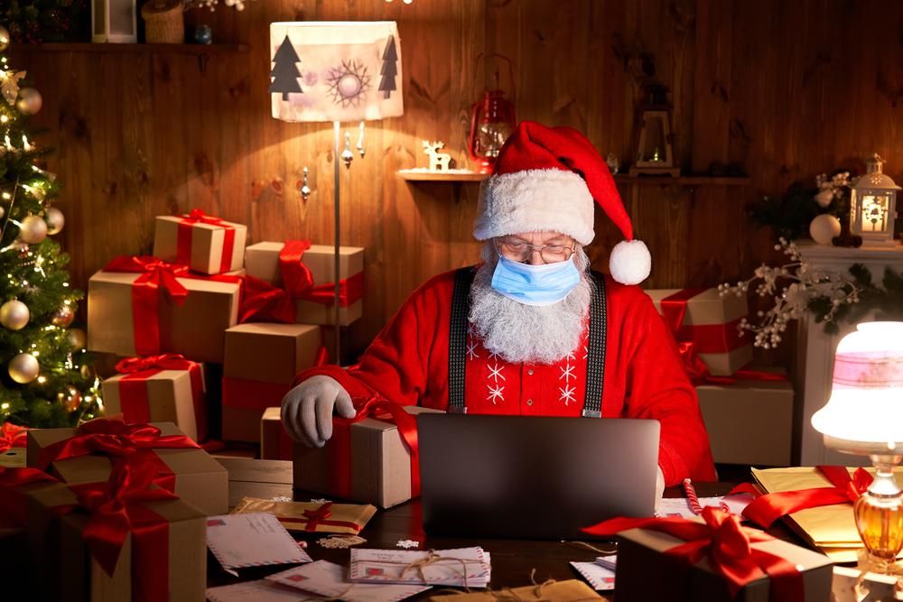 A karácsonyfával és ajándékdobozokkal körbevett Télapó maszkban nézi a laptopján a gyerekek kívánságait
