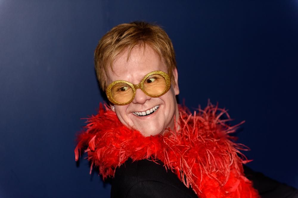 Elton John piros boával a nyaka körül, aranyozott szemüvegben mániákusan vigyorog, miután megtudta, hogy nyilvánosságra hozták a lakcímét