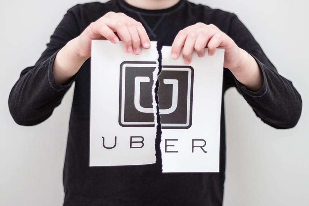 Egy fekete felsős férfi egy fehér fal előtt széttép egy papírt, amelyen az Uber logója és neve látható 