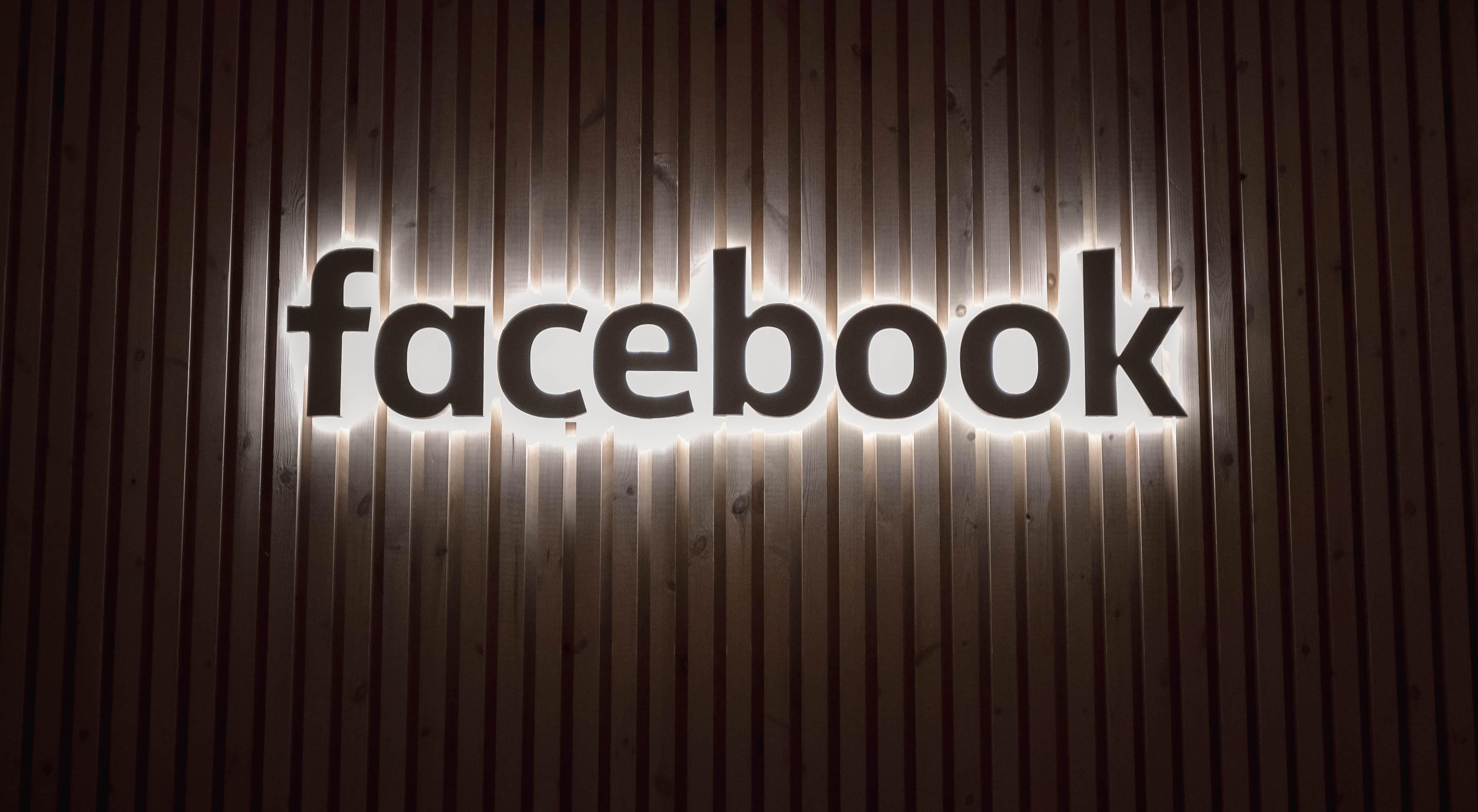 A Facebook logója fehér fénnyel kivilágítva egy falon