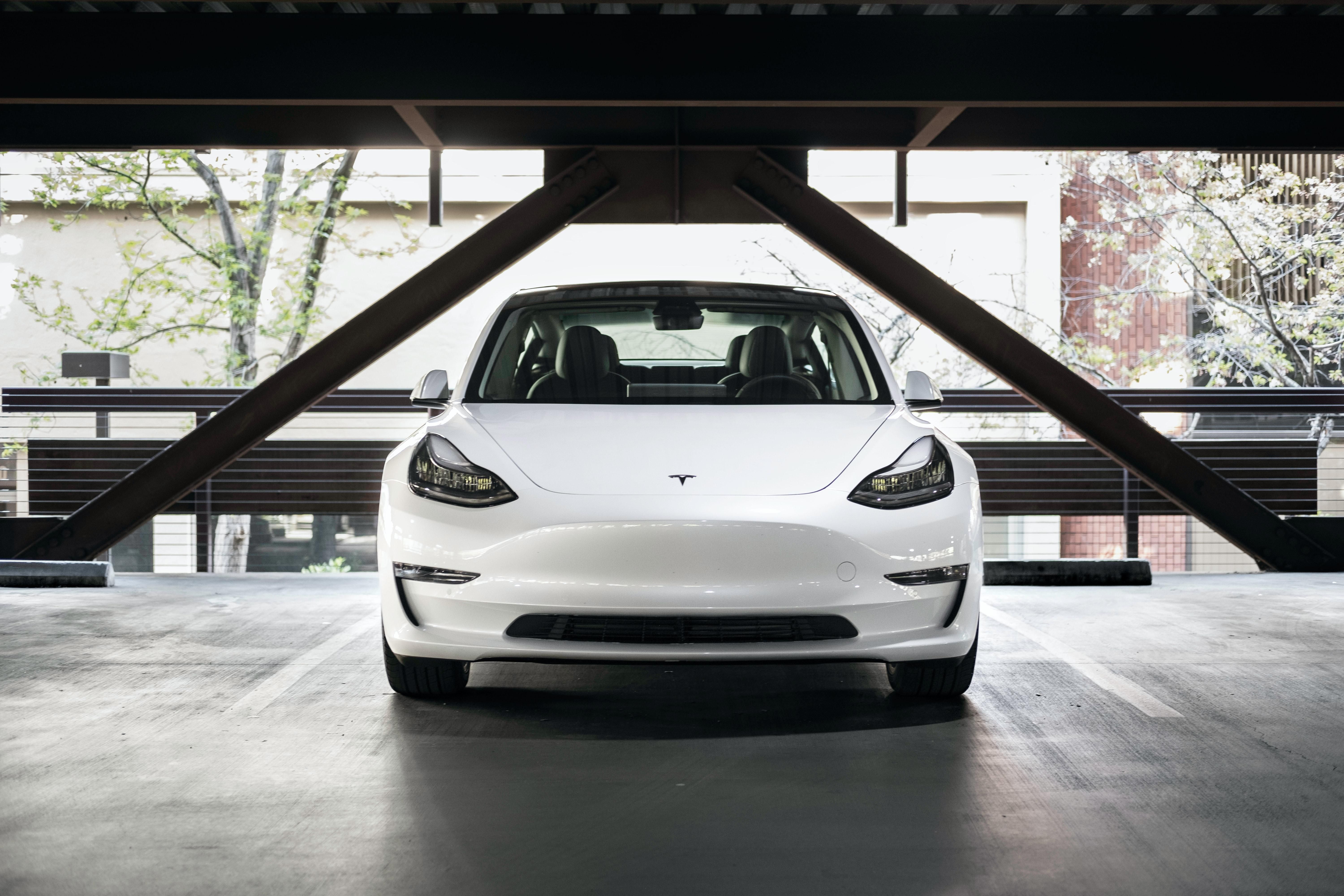 Fehér színű Tesla Model 3 áll egy parkolóház parkolójában nappal