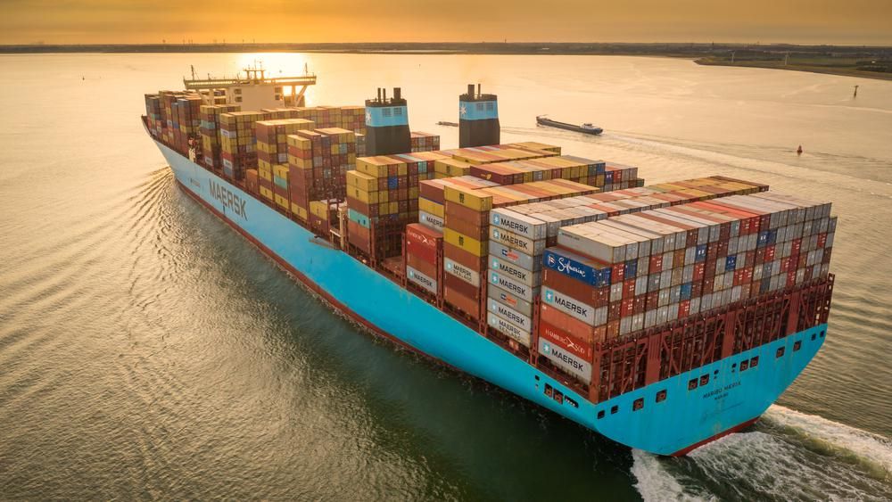A Maersk konténerszállító társaság kék színű konténerhajója konténerekkel megpakolva szeli az óceán vizét naplementében
