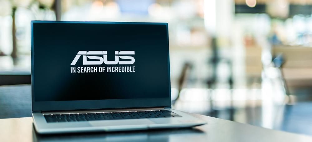Egy Asus laptop van a képen, amely egy asztalon található, a képernyőn az Asus logója és mottója látható, a háttér homályos