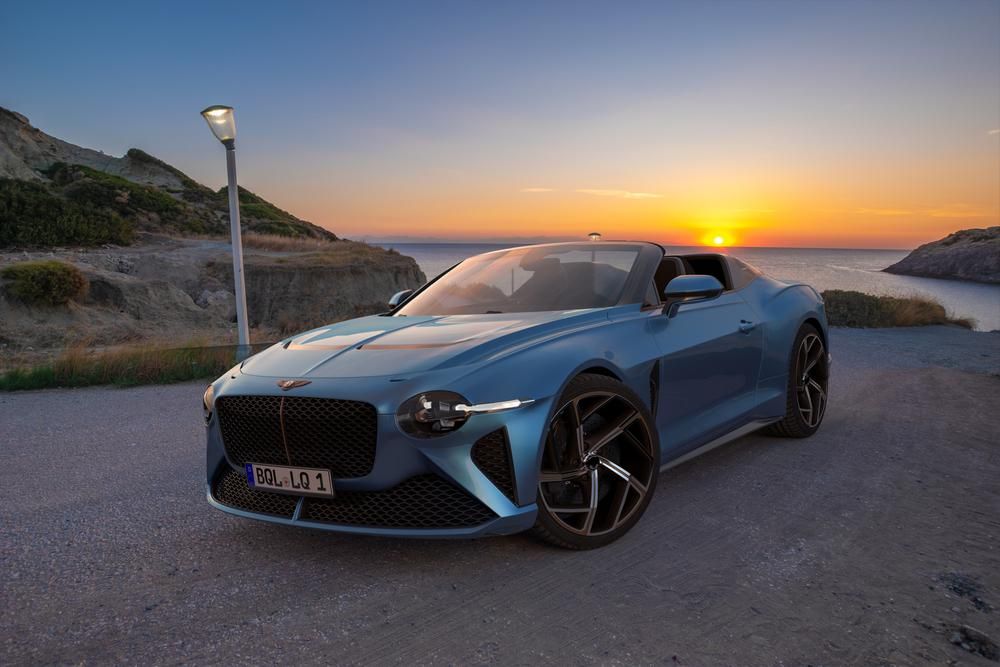 Kék színű Bentley luxusautó parkol egy tengerpart közelében az úton, naplementében