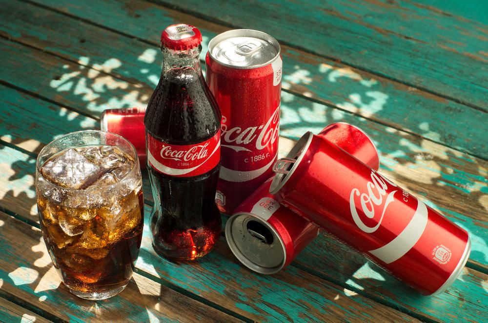 Coca-Colás üveg és dobozok, illetve egy pohár kóla egy kopott fafelületen