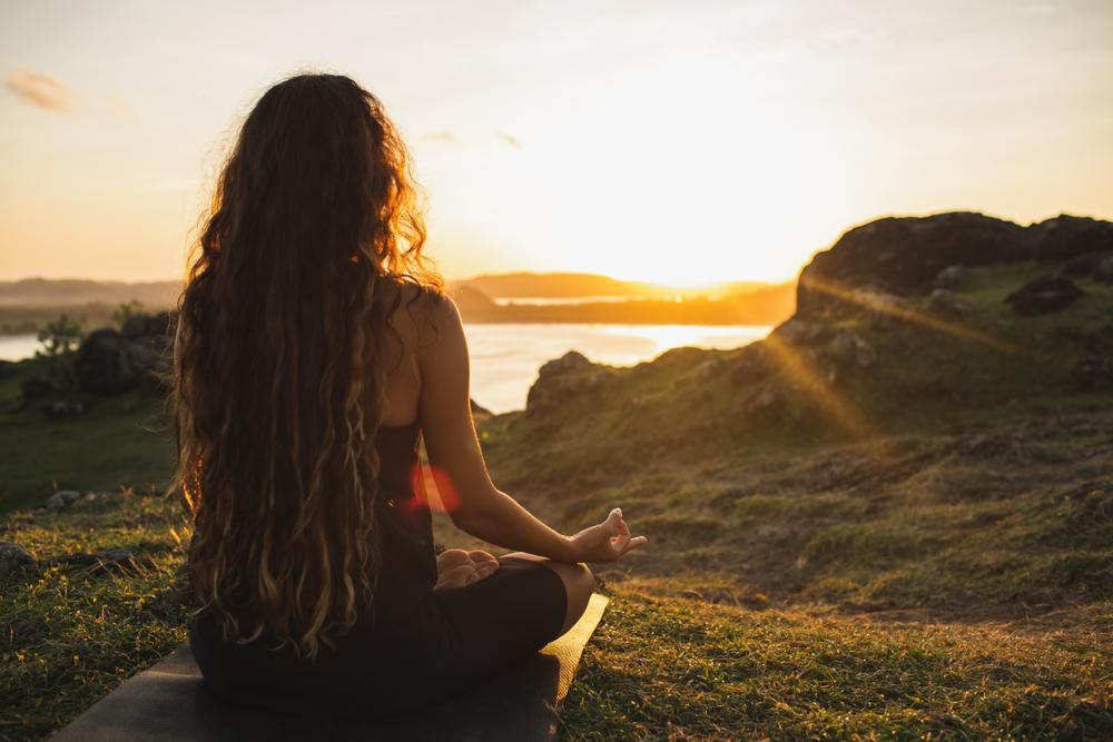 Melírozott hajú lány meditál egy tengerparton a naplementében egy pénteki napon, ugyanis a munkahelyén csupán négy napot kell dolgoznia egy héten, ezért pénteken is meditálhat