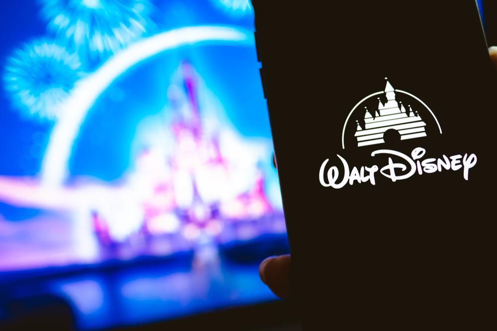 A Walt Disney logója egy okostelefon fekete képernyőjén, a háttérben a Walt Disney kastély sziluettje látható