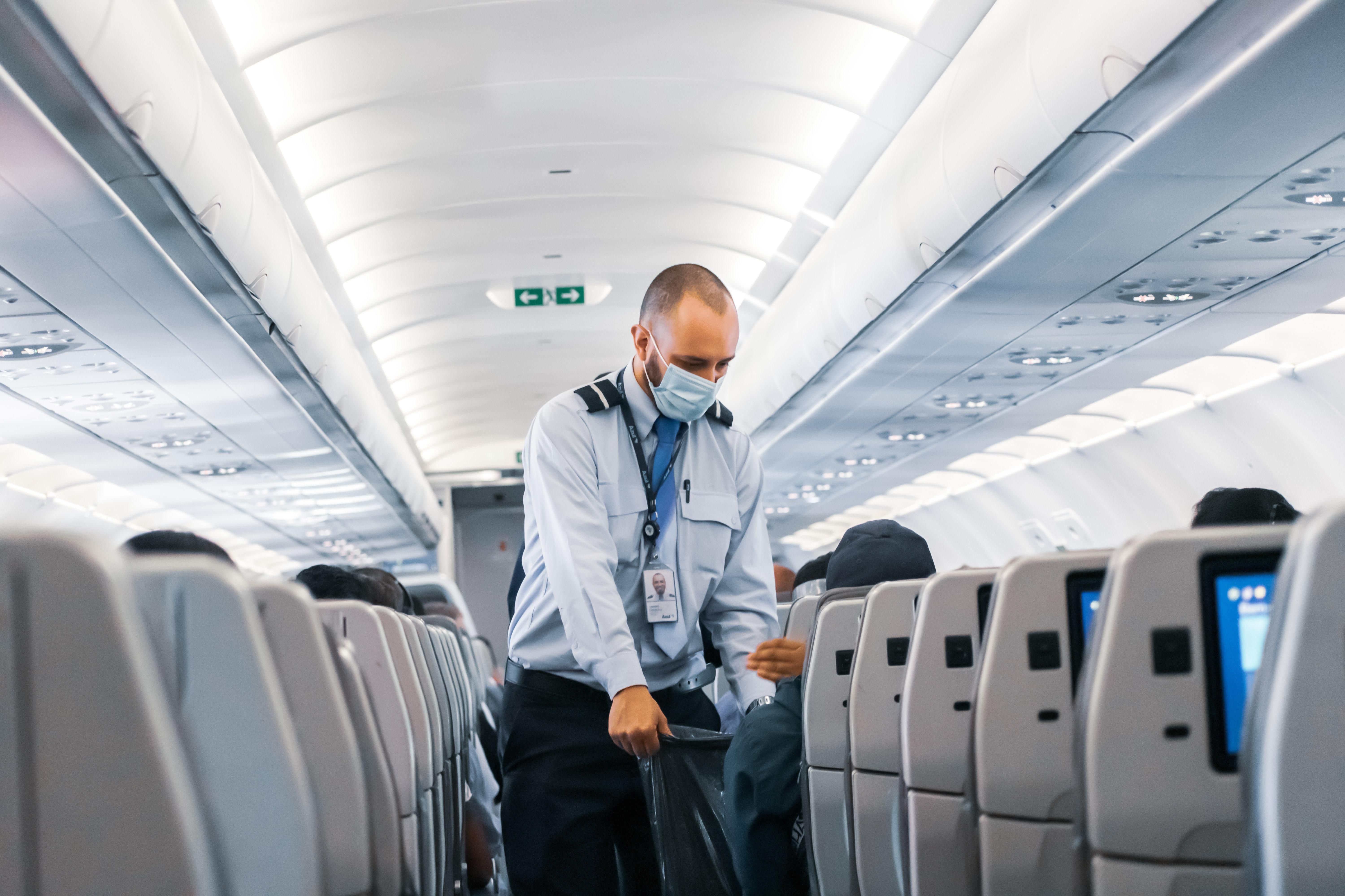 A Delta Air Lines légitársaság kék inges légi tisztje, munkavállalója kék maszkban járja a repülőt és gyűjti a szemetet egy fekete szemeteszsákba