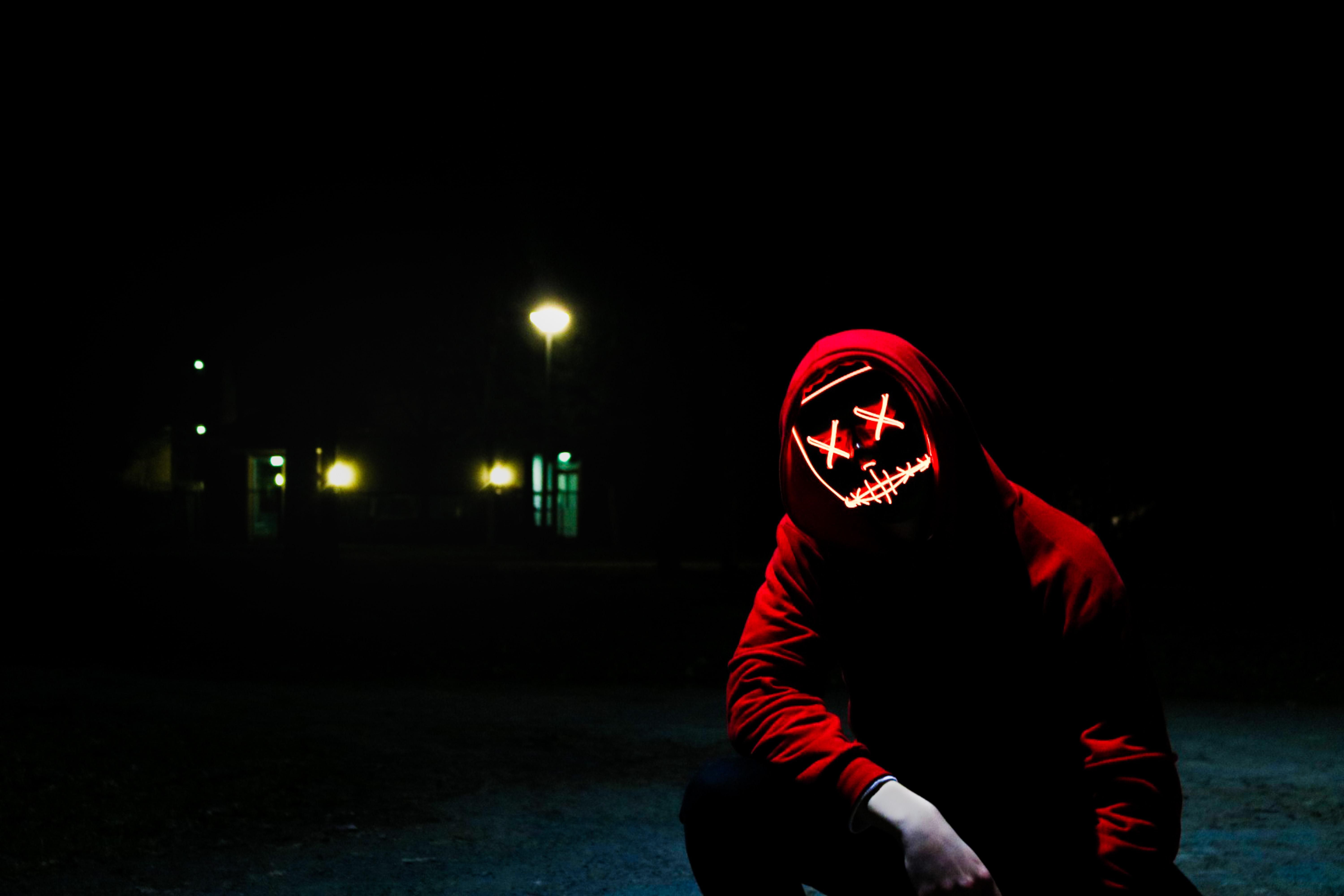 Piros pulóveres hacker guggol éjszaka az utcán, egy pirosan világító maszk van az arcán