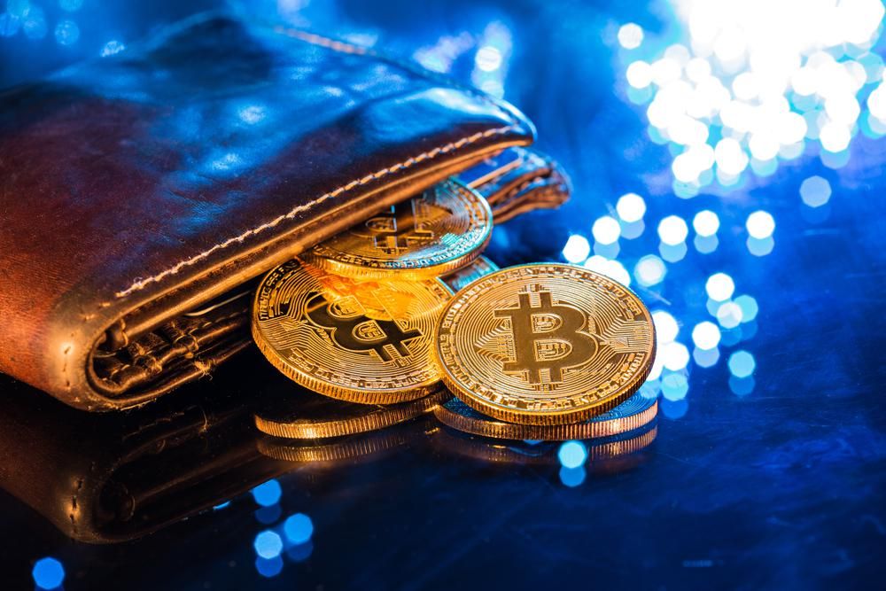 4 darab bitcoin-érme csúszott ki egy barna bőr pénztárcából egy csillogó, kék felületre