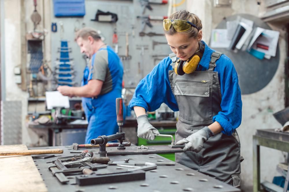 Külföldi vendéhmunkások dolgoznak egy német gyárban, egy szőke nő és egy nagydarab férfi, mindketten munkaruhában vannak