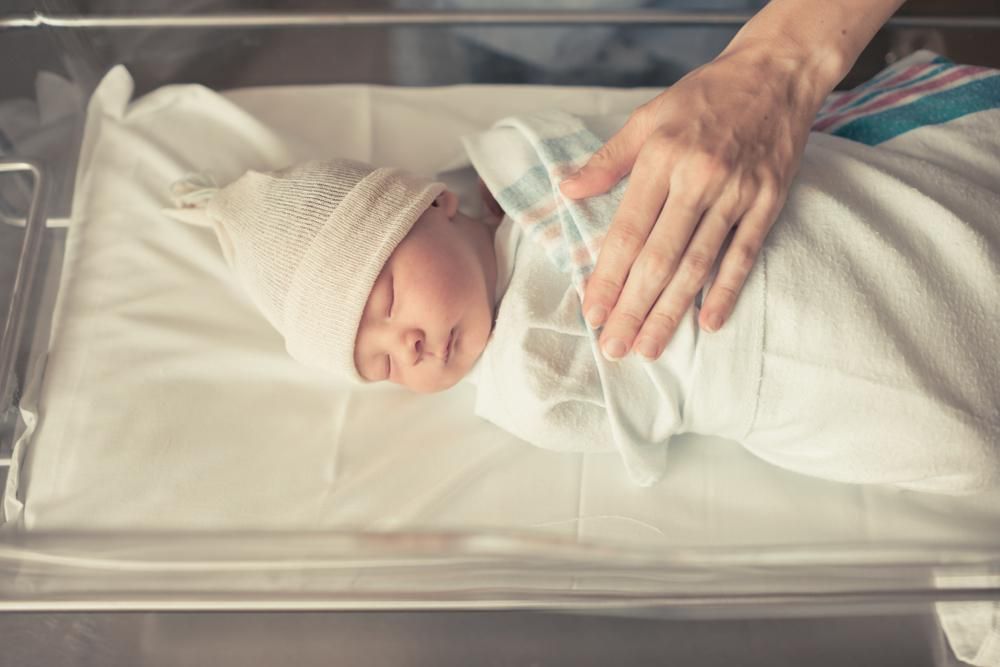 Újszölött csecsemő egy kórházi ágyon, az anyukája a mellkasára teszi a kezét, Dél-Koreában 2 millió wont kapnának