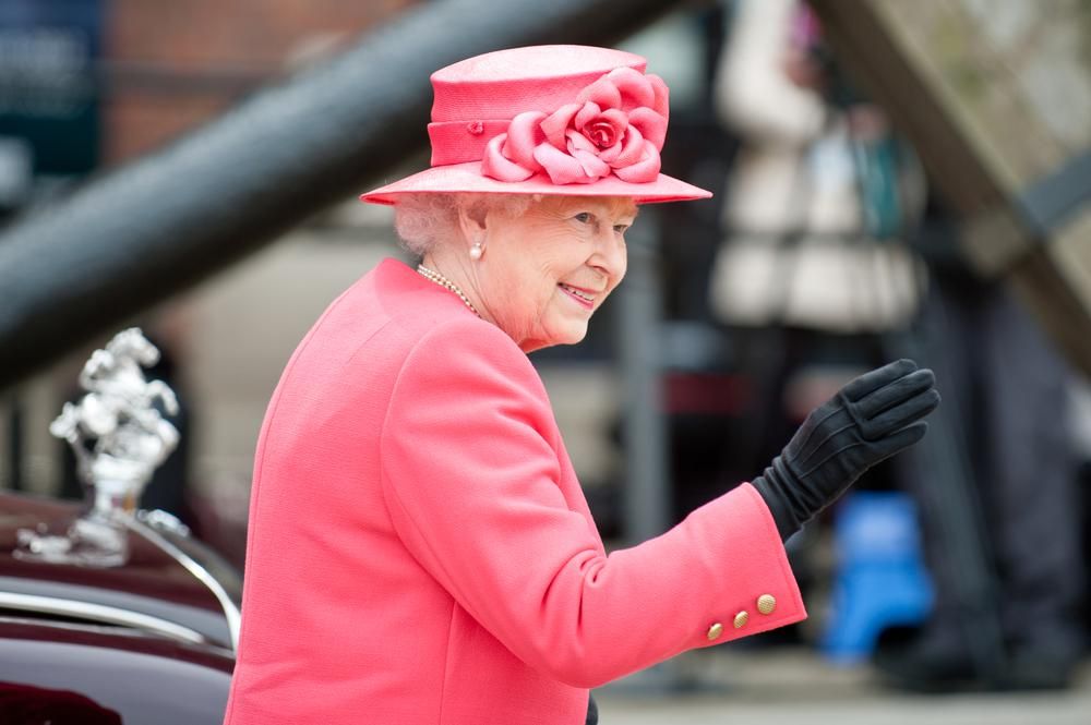II. Erzsébet királynő rózsaszín kosztümben, rózsaszín kalapban integet alattvalóinak