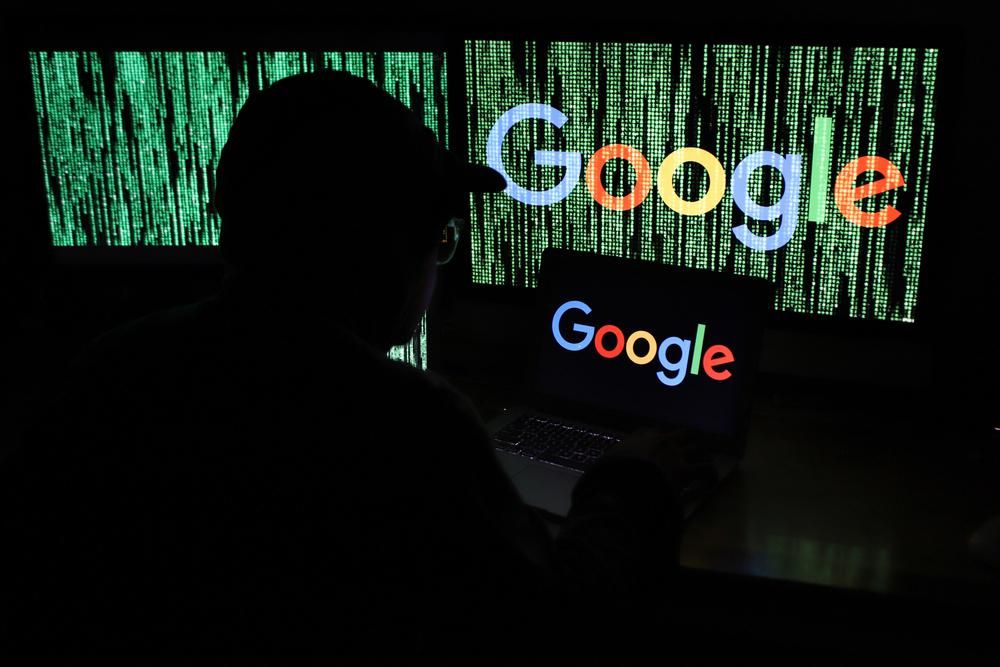 Adatvédelmi szakember baseball sapkában egy sötét szobában figyeli a Google-t, amelynek logója több képernyőn is látszik