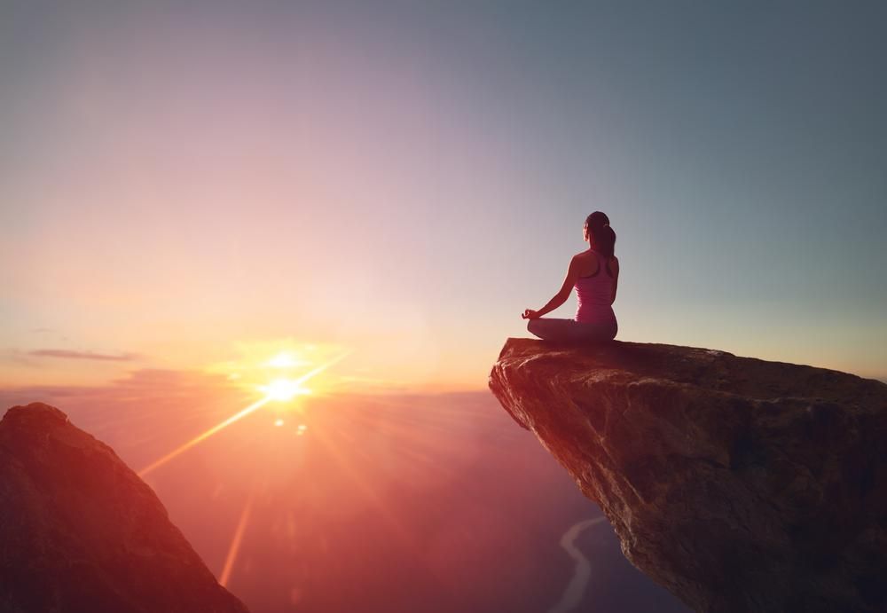 Egy nő egy sziklaszirten meditál a napfelkeltében, a négynapos munkarend mellett erre is van ideje