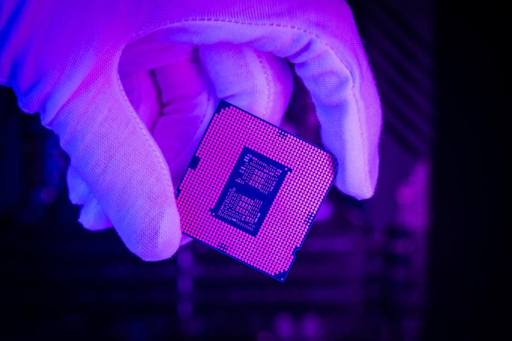 Az Intel chipjét fogja a kezében egy fehér kesztyűs szakember egy lila környezetben