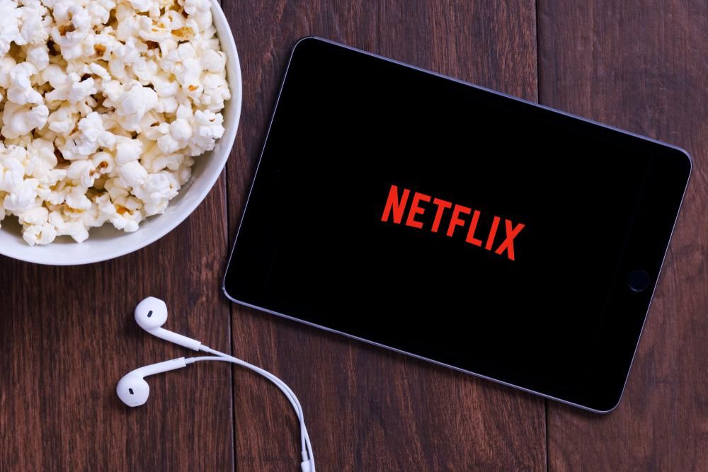 A Netflix logója egy tableten, mellette egy tál popcorn és egy fülhallgató