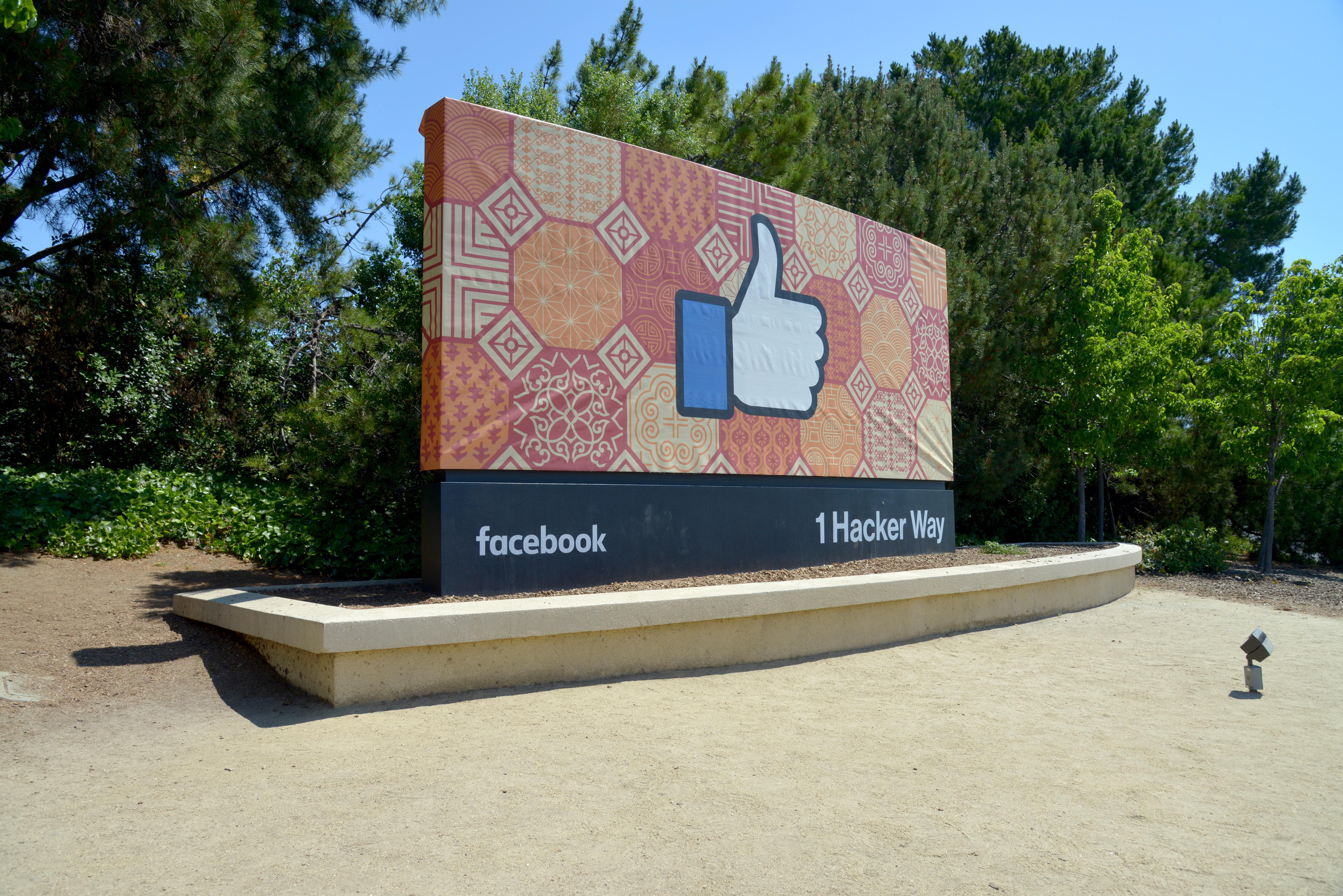 A Facebook logója egy hirdető táblán, amin egy nagy lájk, kedvelés reakció látható, napos idő van