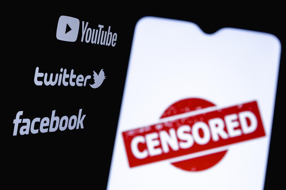 A Facebook, a YouTube és a Twitter logója egy okostelefon mögött, melynek képernyőjén a cenzúrázva felirat látható angolul