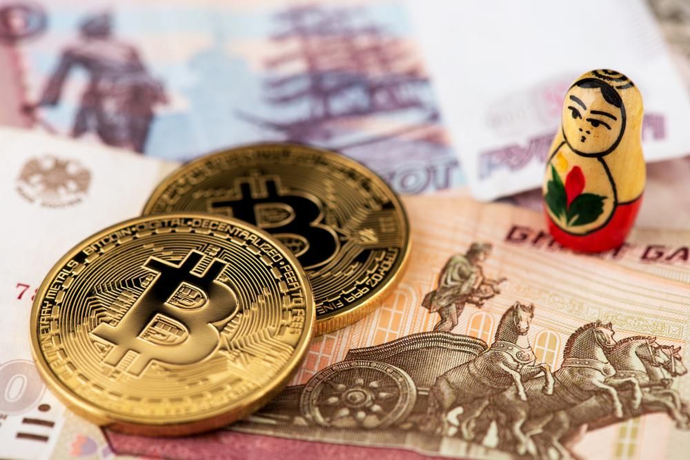 Két bitcoin érme egy orosz matrjoska-baba mellett, rubeleken