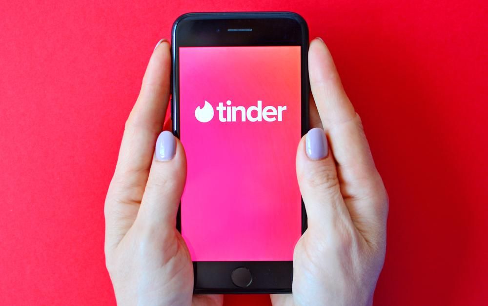 A Tinder tárkereső logója egy telefon képernyőjén, ami egy nő kezében van