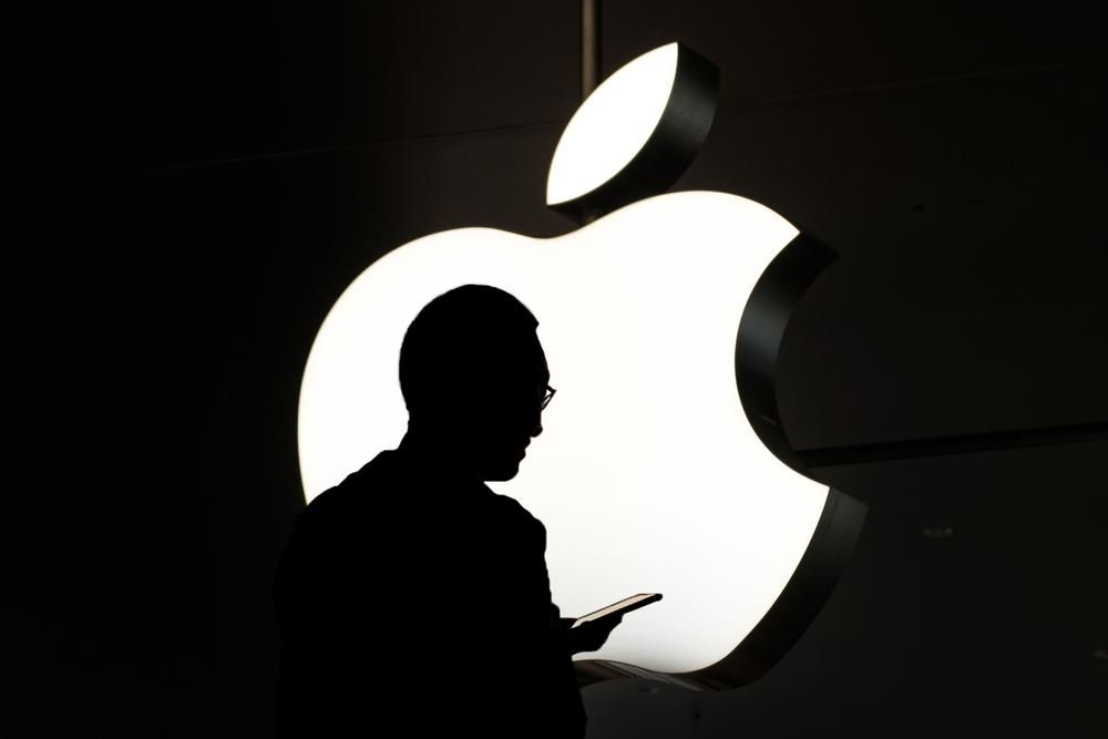 A világ legértékesebb vállalatának, az Apple-nek a logója, előtte egy munkavállaló telefonozik