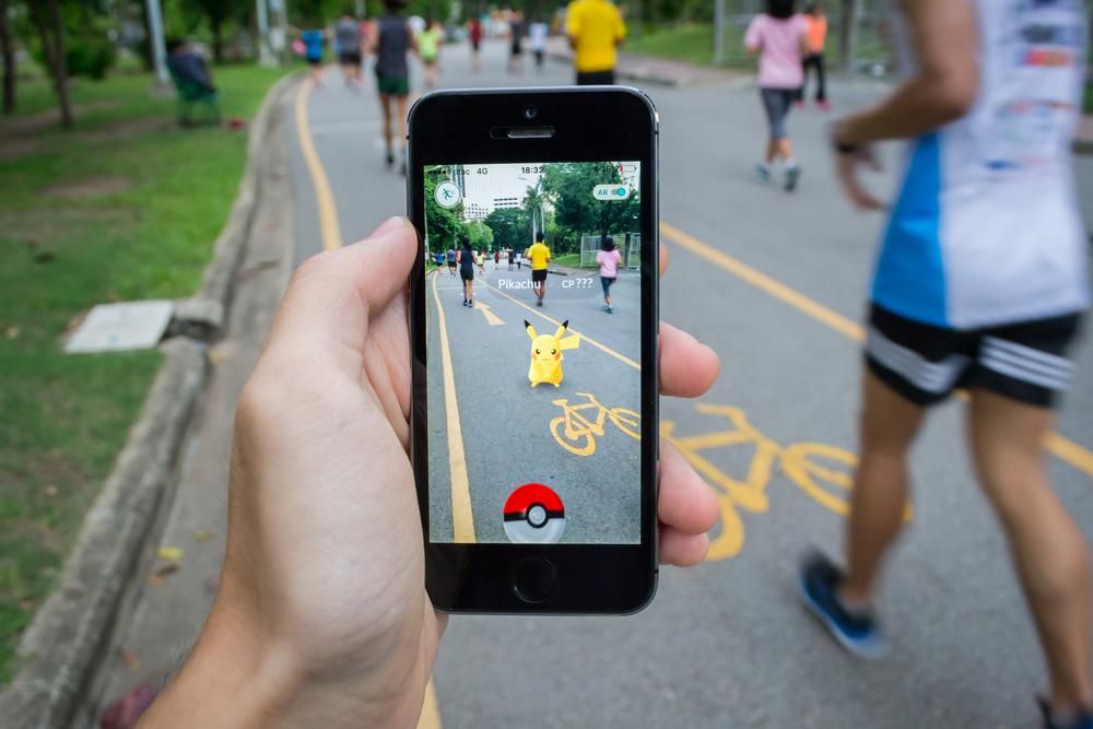 Egy ember a Pokémon Go-val játszik egy futóversenyen, egy Pikachu látható telefonja képernyőjén