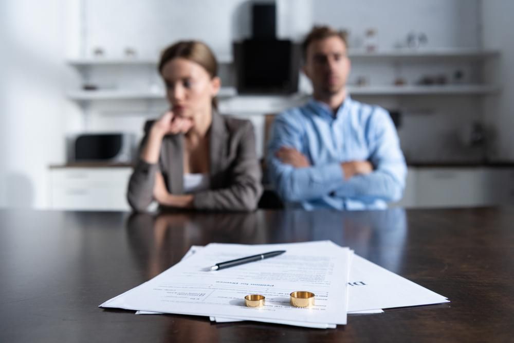 Elvált nő és férfi ül az ügyvéd előtt a válási papírokkal, amelyeken a gyűrűik vannak, kriptovalutákkal próbálták elrejteni vagyonukat egymás elől