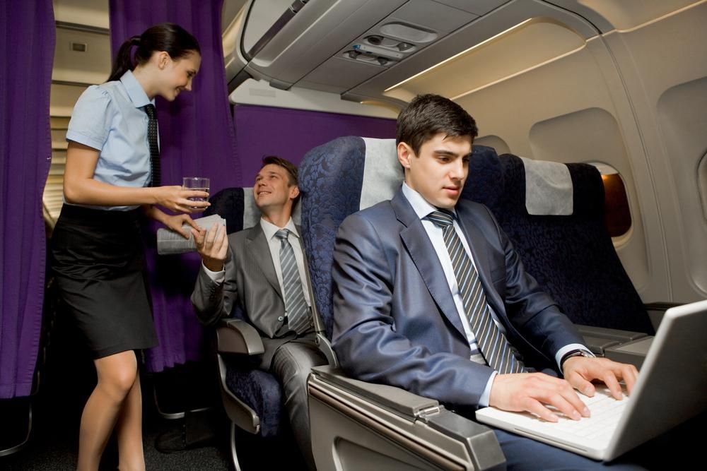 Repülégépen stewardess kiszolgálja az öltönyös utasokat