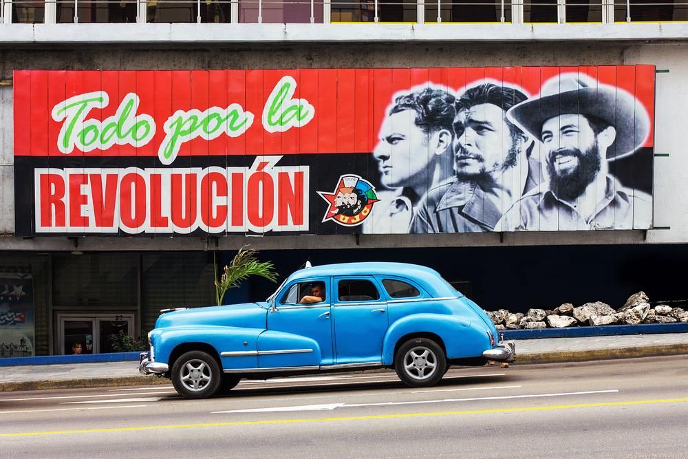 Klasszikus kék taxi Havannában, forradalmi plakát előtt.