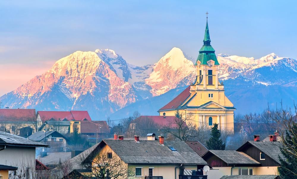 Svájci kisváros templomtoronnyal, háttérben hófödte hegycsúcsokkal