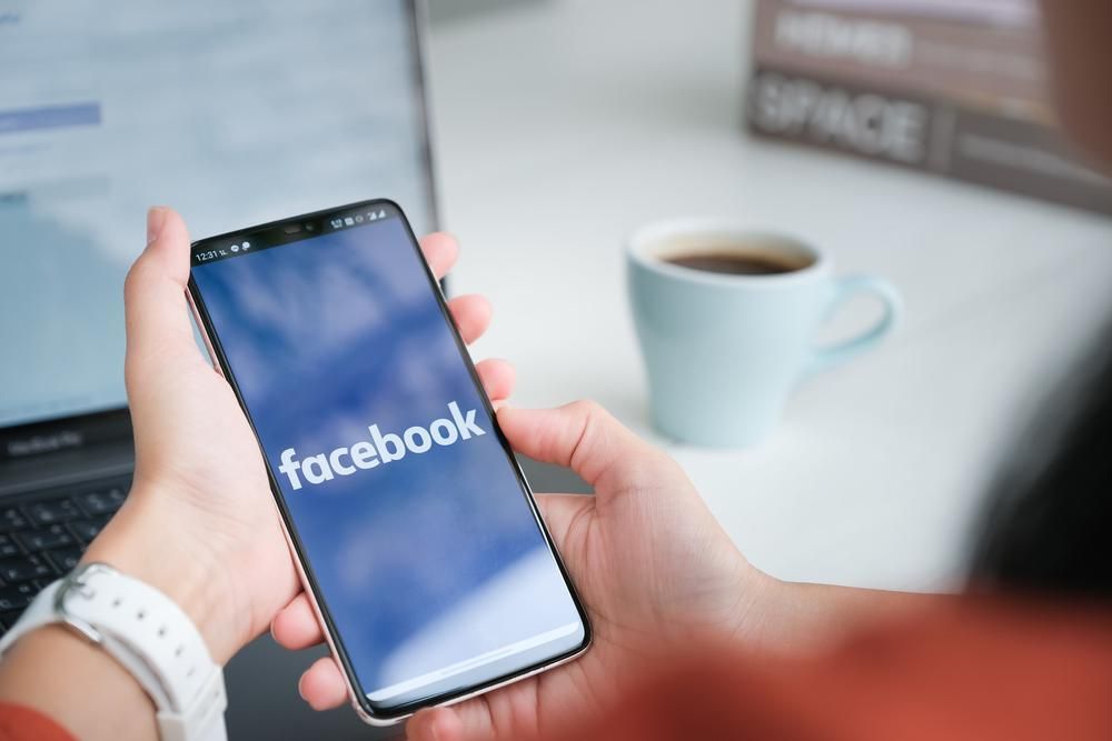Facebook logó egy okostelefon képernyőjén, háttérben egy csésze kávéval