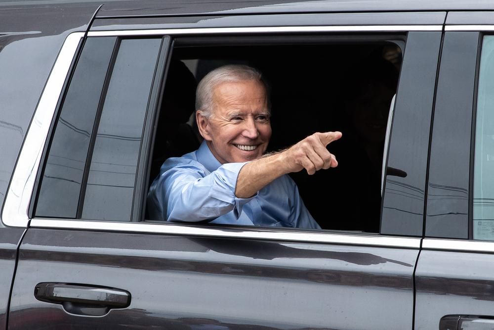 Joe Biden egy autóban mosolyog, lehúzott ablakból integet