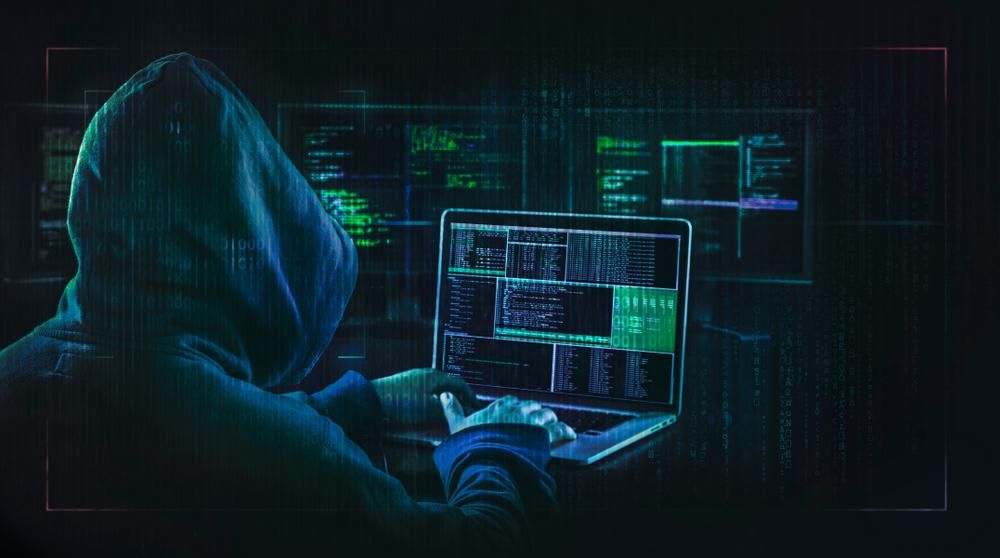 Hacker kapucniban laptoppal és monitorokkal