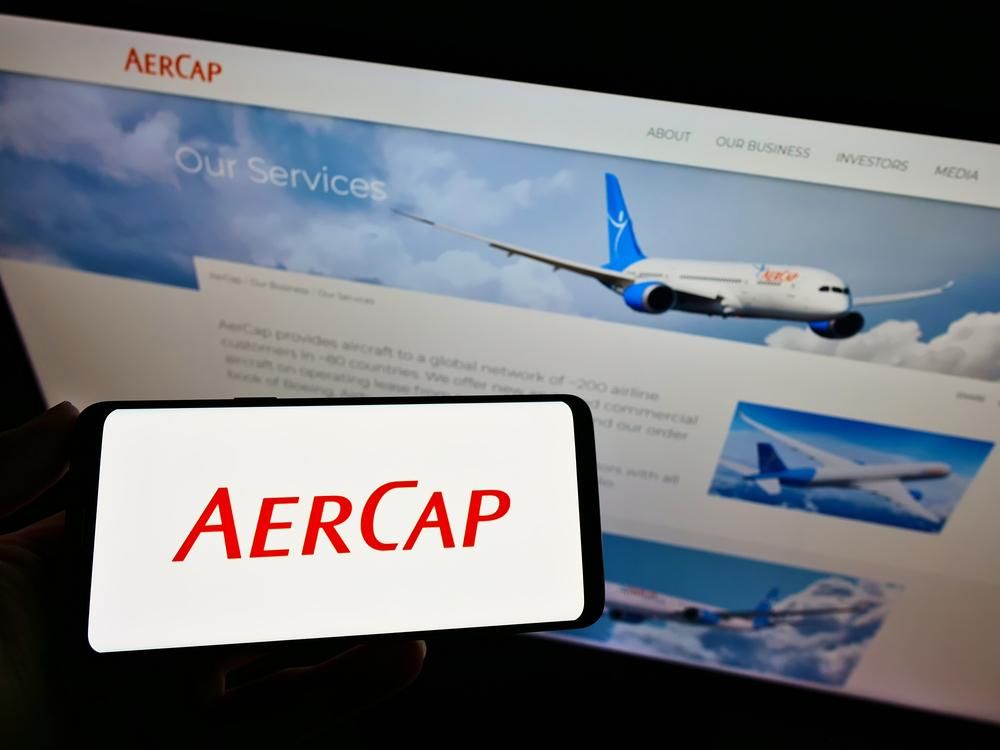 AerCap logó okostelefonon háttérben képernyő repülőgépekkel
