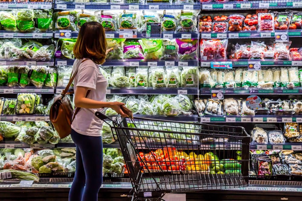 Zöldségespult színes zöldségekkel fiatal nő bevásárlókocsival