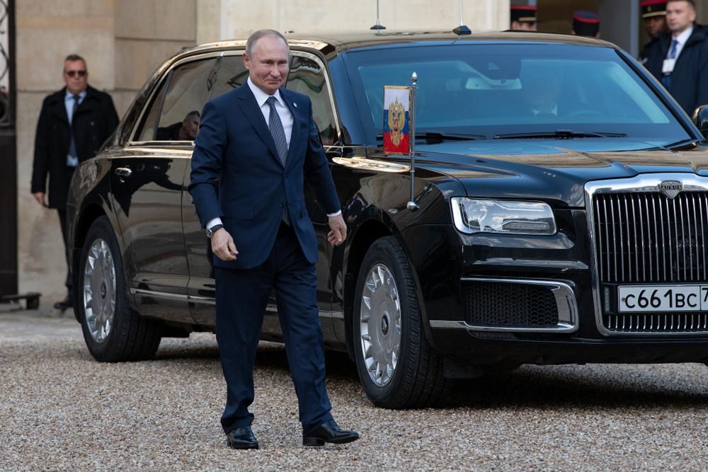 Putyin elnök egy páncélozott  autó mellett sétál, magabiztos léptekkel