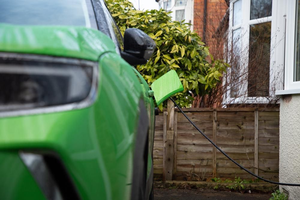Zöld elektromos autó egy ablak alatt töltődik