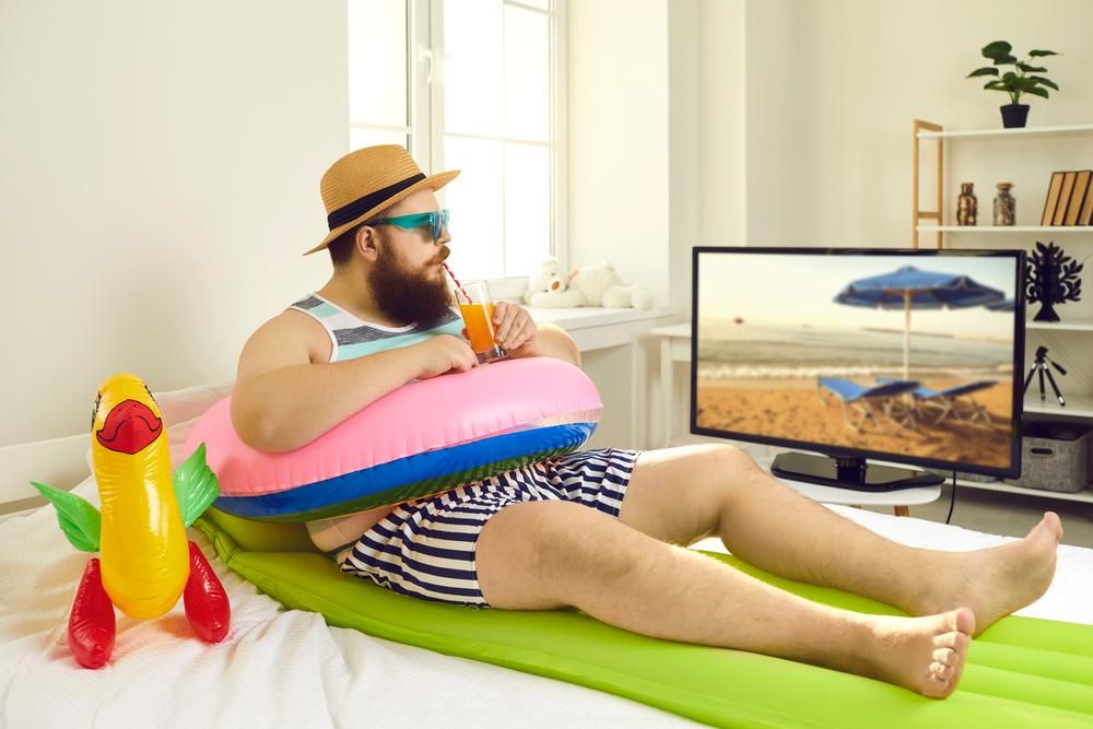 Férfi otthon gumimatracon nézi a tévében a tengerpartot